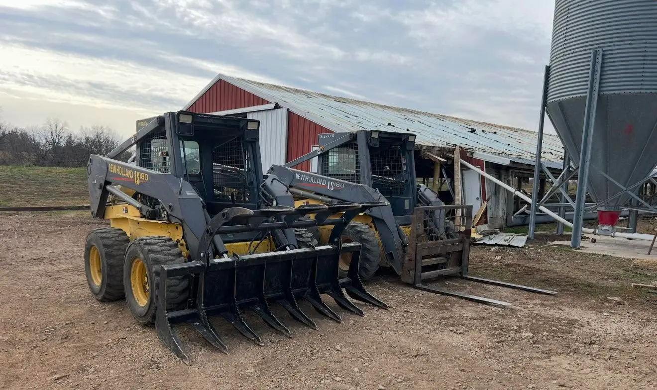 Two skid-steer loaders beside an agricultural building